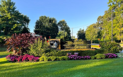 Sign for Inniswood Metro Gardens surrounded by colorful flowers and greenery on a sunny day.