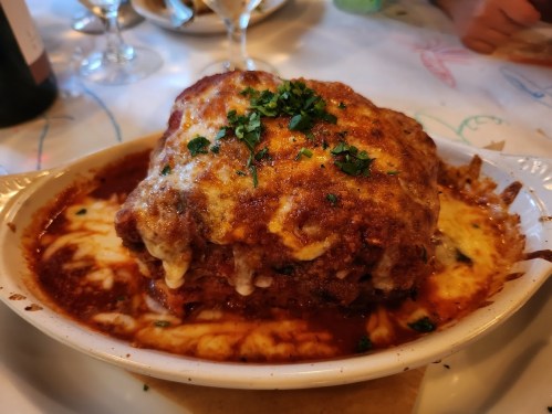 A hearty serving of lasagna topped with melted cheese and garnished with parsley, served in a white dish.