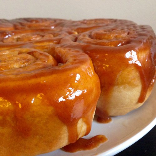 Close-up of freshly baked cinnamon rolls drizzled with glossy caramel sauce on a white plate.