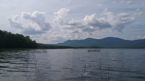 A serene lake surrounded by mountains under a cloudy sky, with gentle ripples on the water's surface.