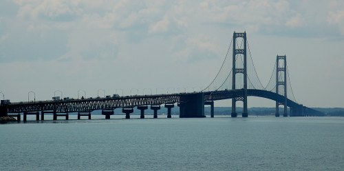 A large suspension bridge spans a calm body of water under a cloudy sky.