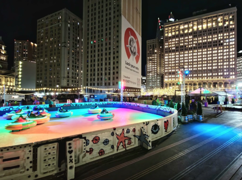 Colorful bumper cars on an illuminated rink at night, surrounded by city buildings and festive lights.