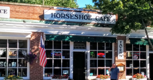 A brick building with a sign reading "Horseshoe Cafe," featuring an American flag and neon lights in the windows.