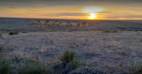 A serene sunset over a vast, arid landscape with sparse vegetation and distant hills.