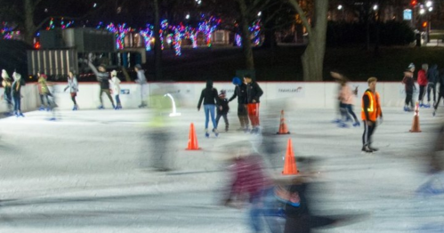 A busy ice skating rink at night, with skaters in motion and colorful lights in the background.
