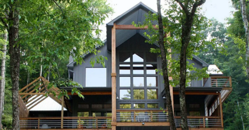 Modern cabin nestled among trees, featuring large windows and a stylish design.