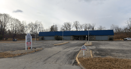 Exterior view of a vacant building with a blue roof, surrounded by an empty parking lot and signs for Lucky Strike Lanes.