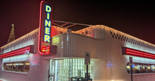 A brightly lit diner at night, featuring neon signage and a festive holiday decoration on top.