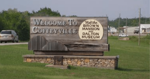 Welcome sign for Coffeyville, featuring attractions like the Brown Mansion and Dalton Museum. Green grass and trees in background.