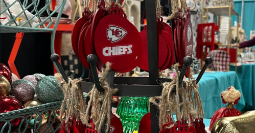 A display of red Kansas City Chiefs ornaments hanging on a rack at a market or craft fair.