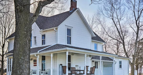 A charming white two-story house with a porch, surrounded by bare trees and a clear sky.