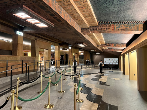 Interior view of a spacious lobby with decorative ceilings, patterned floors, and a queue barrier.