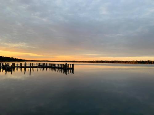 A calm lake at sunset, with a wooden pier extending into the water under a cloudy sky.