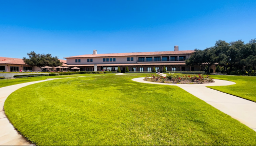 A spacious green lawn with a curved pathway leading to a large building under a clear blue sky.