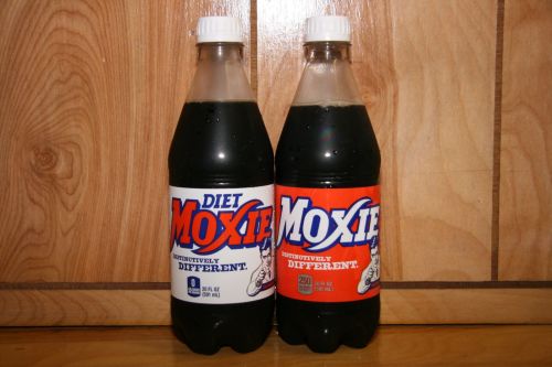 Two bottles of Moxie soda, one labeled "Diet" and the other regular, against a wooden background.