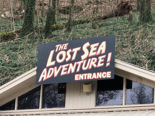 Sign for "The Lost Sea Adventure" with "ENTRANCE" displayed prominently, set against a wooded background.