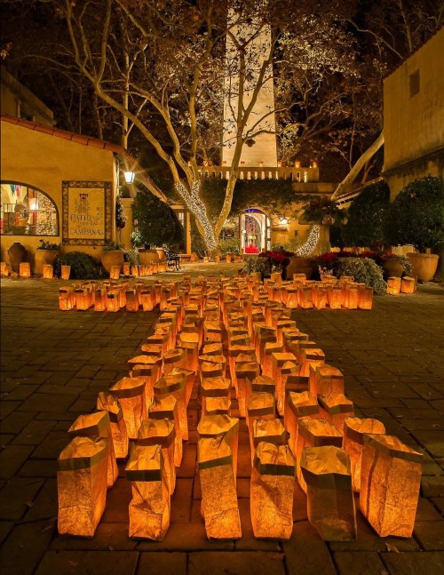 A serene courtyard illuminated by glowing paper lanterns, with a tall tower and trees in the background.