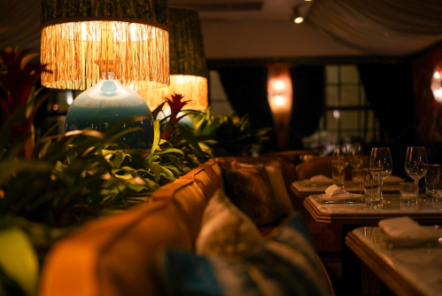 Cozy restaurant interior with warm lighting, lush greenery, and elegantly set tables.