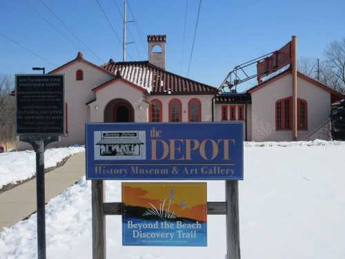 Sign for the Depot History Museum & Art Gallery, featuring a historic building with a tile roof and snowy surroundings.