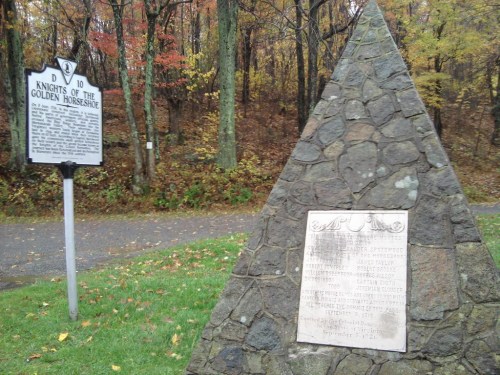 A stone monument with a plaque beside a historical marker in a wooded area with autumn foliage.