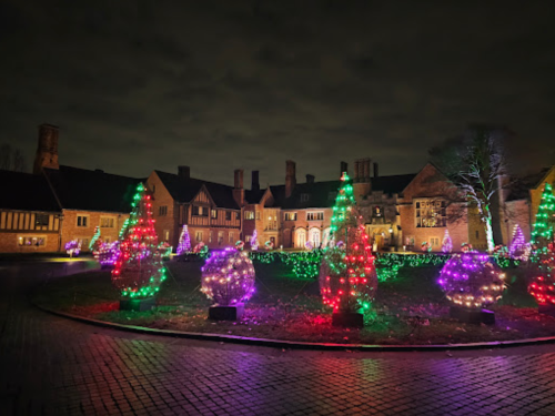 A beautifully lit mansion surrounded by colorful Christmas trees at night, creating a festive atmosphere.