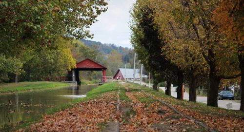A scenic canal lined with trees and autumn leaves, featuring a red covered bridge in the background.