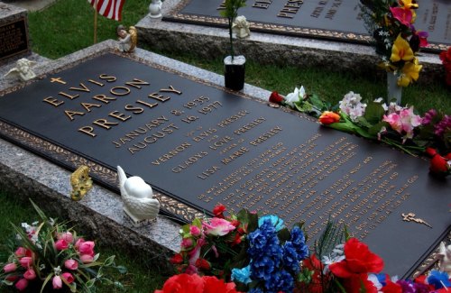 Grave of Elvis Presley, featuring a bronze plaque and colorful flowers, located in a cemetery.