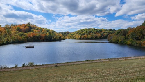 A serene lake surrounded by colorful autumn trees under a partly cloudy sky.