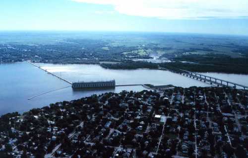 Aerial view of a river, dam, and surrounding landscape with a bridge and residential area below.
