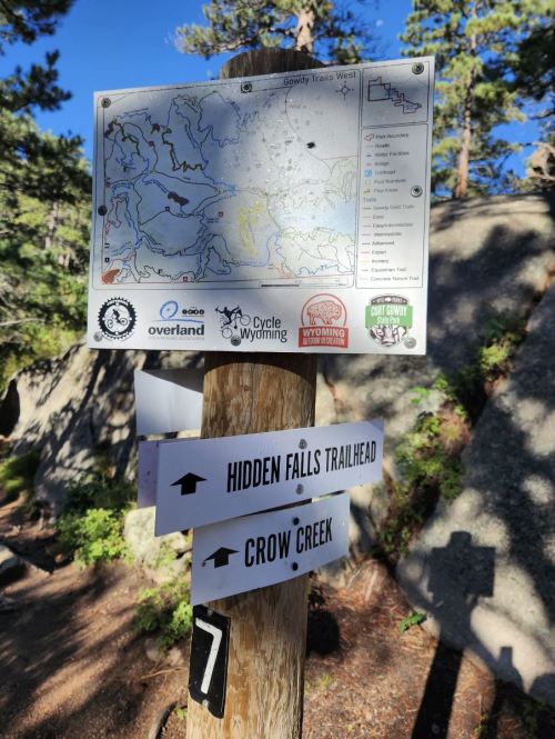 Trail signpost with a map and directions to Hidden Falls Trailhead and Crow Creek, surrounded by trees and rocks.