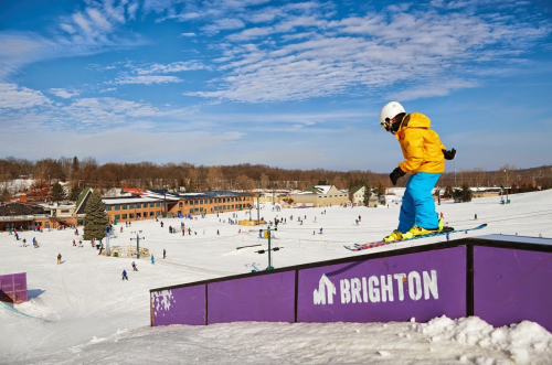 A skier in a yellow jacket descends a ramp at Brighton ski resort, surrounded by snow and other skiers.