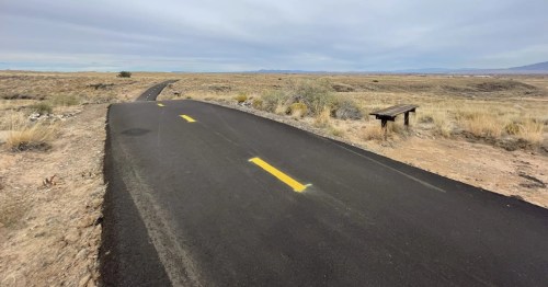 A bench sits next to a paved trail in the middle of a New Mexico desert.