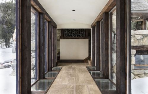 A modern hallway with large windows, stone walls, and wooden accents, featuring a snowy landscape outside.