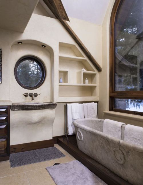 A modern bathroom featuring a round window, stone sink, and a freestanding tub with white towels neatly arranged.