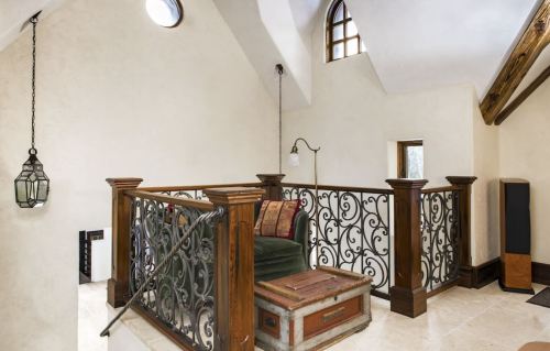A cozy loft area with a decorative railing, a green chair, and a vintage trunk, featuring soft lighting and wooden beams.