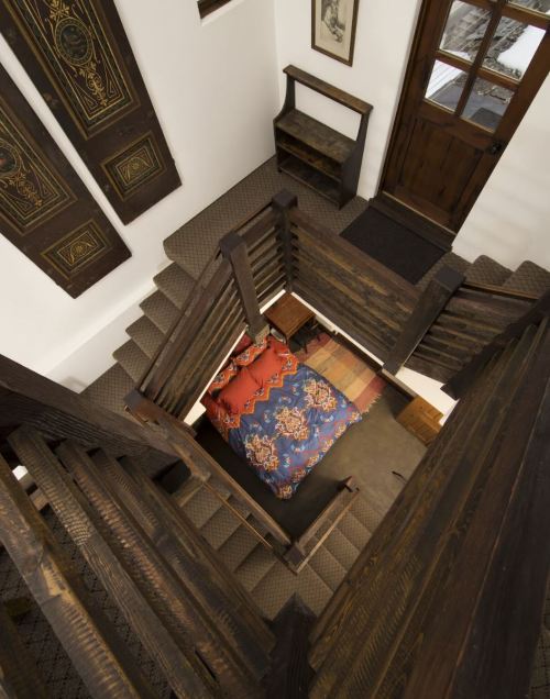 Aerial view of a cozy bedroom with a colorful quilt, surrounded by wooden stairs and decorative wall panels.