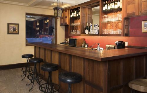 A wooden bar with high stools, shelves of bottles, and a warm, inviting atmosphere in a cozy setting.