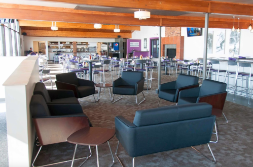Modern dining area with black chairs, wooden accents, and large windows, featuring tables set for guests.