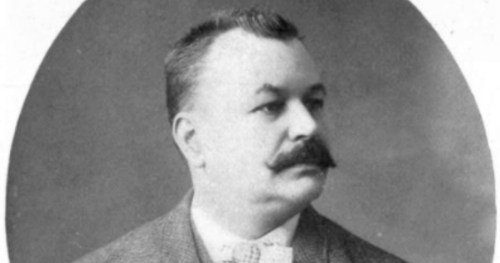 Black and white portrait of a man with a mustache, wearing a suit and bow tie, set in an oval frame.