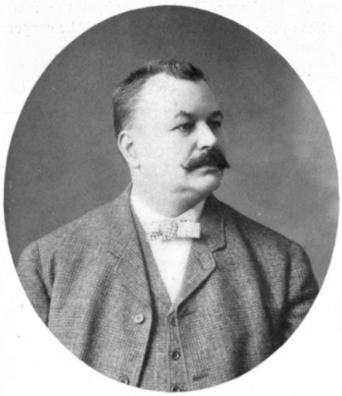 Black and white portrait of a man with a mustache, wearing a bow tie and a suit, set in an oval frame.