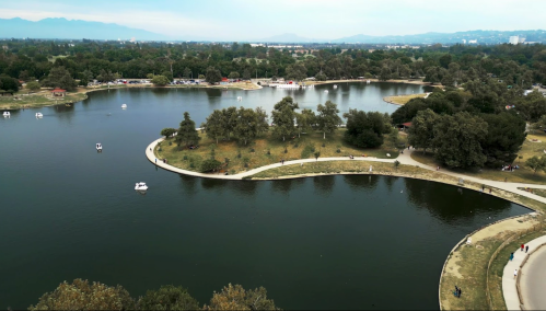 Aerial view of a serene lake surrounded by greenery, with walking paths and small boats on the water.