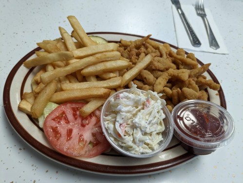 A plate of fried food featuring fries, fried seafood, coleslaw, tomato slices, and dipping sauces.