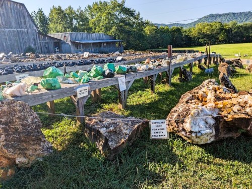 A display of colorful rocks and minerals on tables outdoors, with signs warning visitors to stay back.