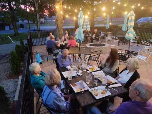 A group of people dining outdoors on a patio, surrounded by string lights and umbrellas, enjoying a meal together.