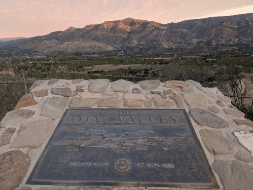 A plaque marking the Ojai Valley, with mountains and a sunset in the background.