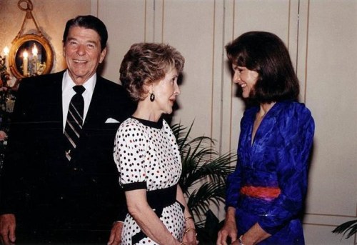 A smiling Ronald Reagan stands with Nancy Reagan and another woman in a formal setting, engaged in conversation.