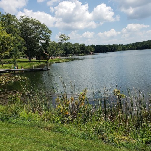 A serene lake surrounded by lush greenery and trees under a partly cloudy sky.