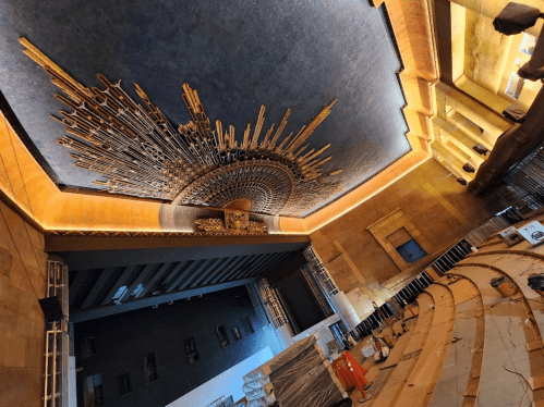 Interior view of a theater under renovation, featuring a dramatic ceiling design and wooden seating.