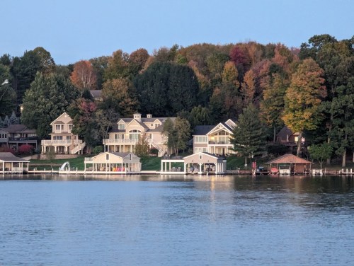 A serene lakeside view featuring homes and colorful autumn trees reflecting in the water.