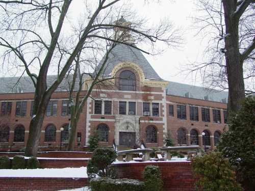 Historic brick building with a large arched window, surrounded by snow-covered trees and a landscaped garden.